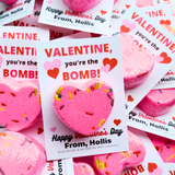 Pink heart-shaped bath bomb with Valentine's Day card and 'you're the Bomb!' text.